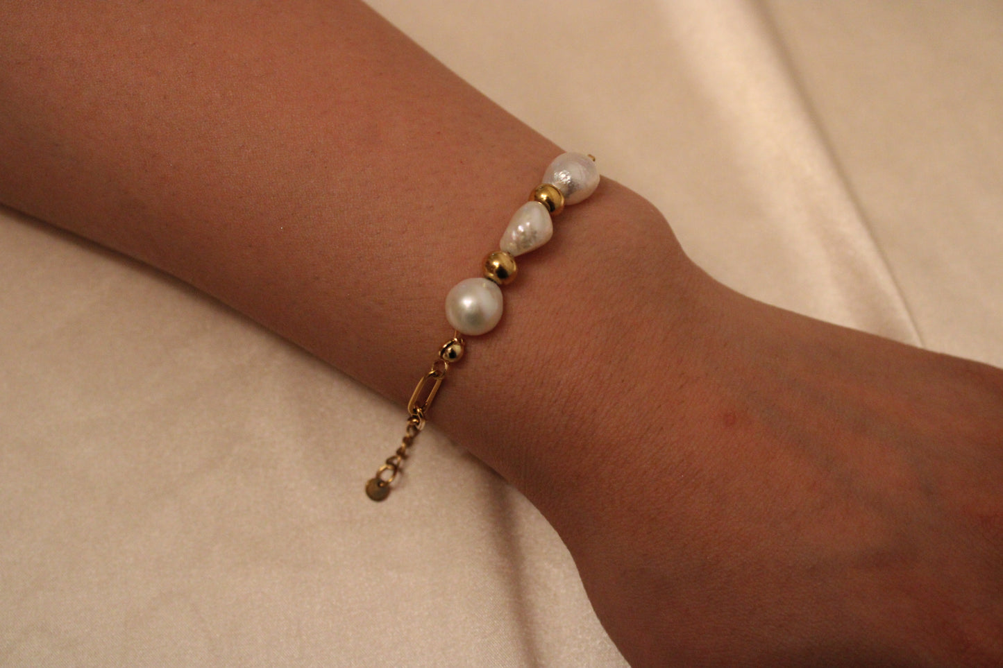 Minimalistische handgemaakte armband met 3 parels en 2 gouden kralen, gedragen aan een pols