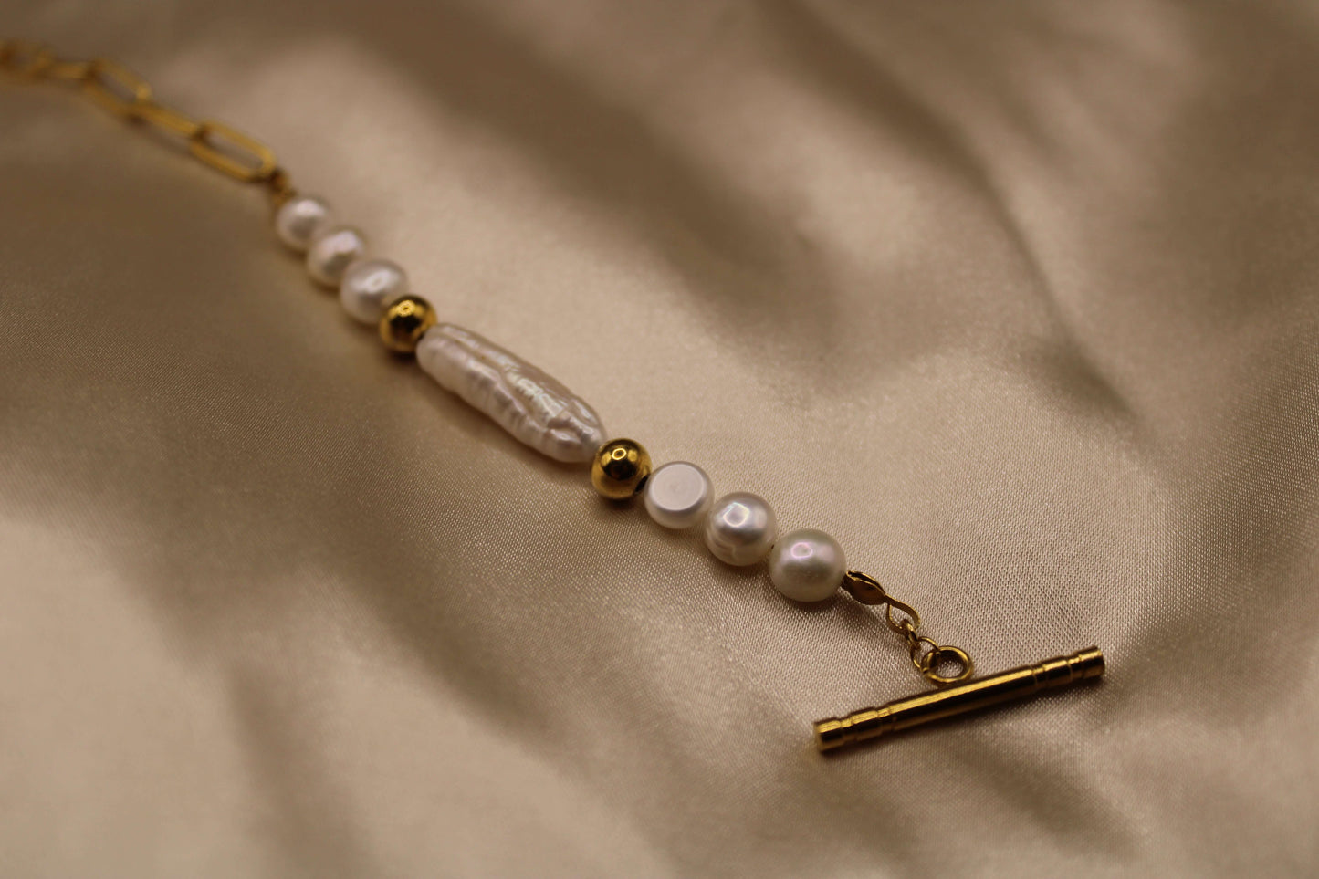 Close-up van een goudkleurig stainless steel ketting met parels en een unieke ronde sluiting