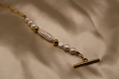 Close-up van een goudkleurig stainless steel ketting met parels en een unieke ronde sluiting
