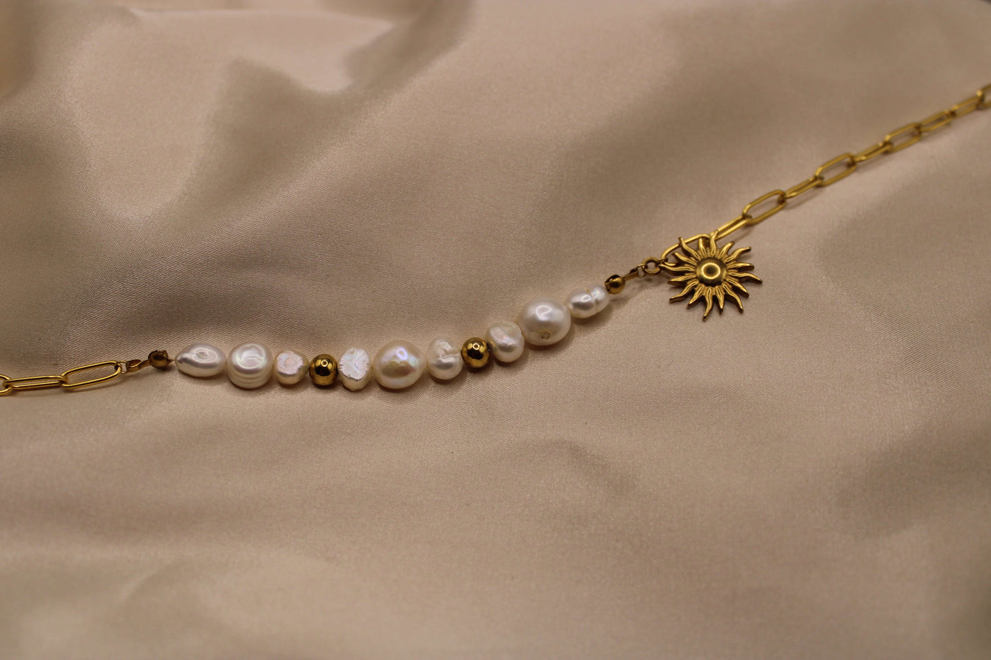Ketting van goudkleurig roestvrij staal met een zonvormige hanger, elegante zoetwaterparels en fijne kralen.
