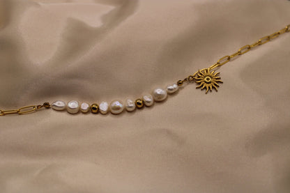 Ketting van goudkleurig roestvrij staal met een zonvormige hanger, elegante zoetwaterparels en fijne kralen.