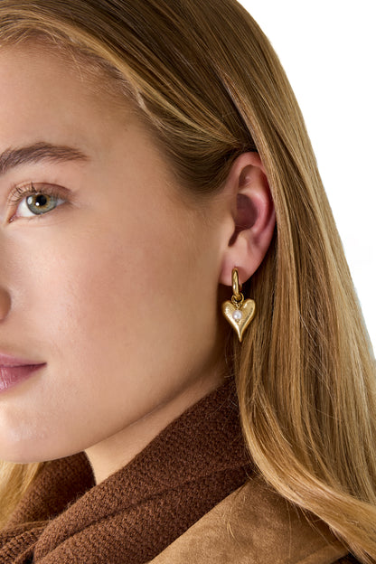 Zijaanzicht van model met goudkleurige hangende hart oorbellen in het oor