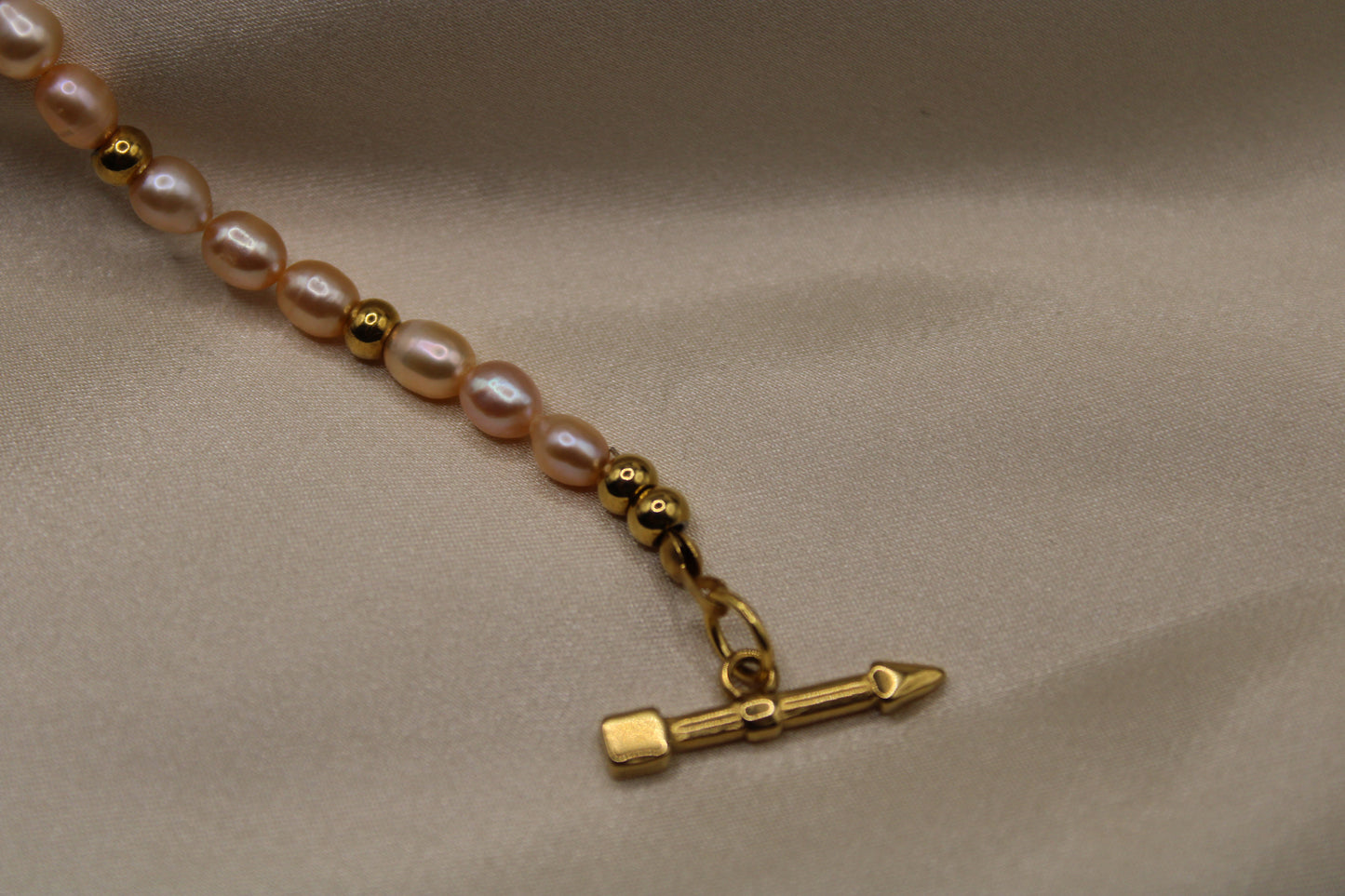 Elegante ketting met roze zoetwaterparels, goudkleurig staal en hartsluiting.
