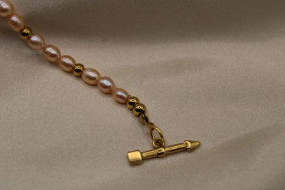 Elegante ketting met roze zoetwaterparels, goudkleurig staal en hartsluiting.
