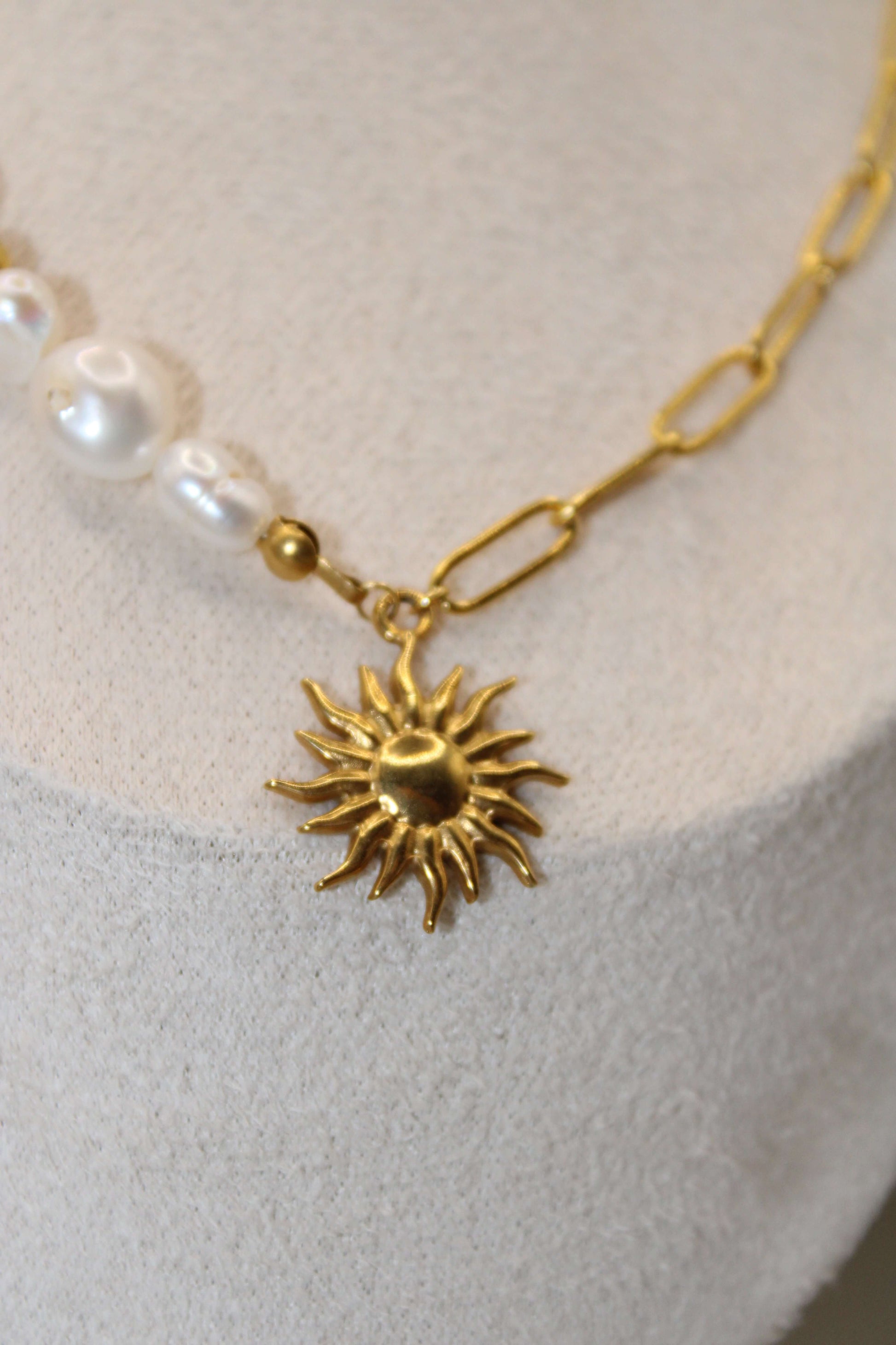 Elegant ontworpen ketting met een zonvormige hanger van goudkleurig staal, afgewerkt met parels en kralen.